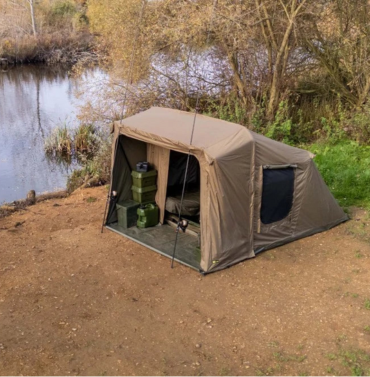 A green Ridgemonkey bivvy tent (bivvy shelter) set up by a river, designed for camping and outdoor activities.